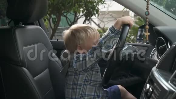 男孩坐在汽车的车轮前想象着他是如何驾驶它的视频的预览图