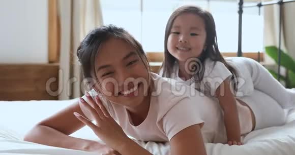 快乐的亚洲妈妈和女儿在床上看摄像机视频的预览图