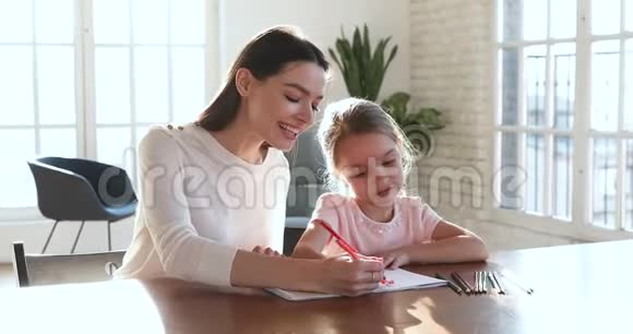 微笑着妈妈教小女孩一起用彩色铅笔画画视频的预览图