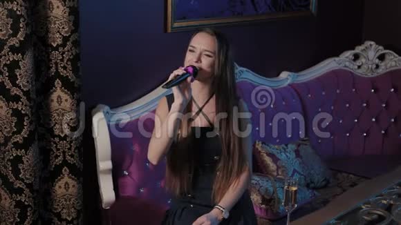 年轻女孩在卡拉OK俱乐部的沙发上对着麦克风唱歌视频的预览图