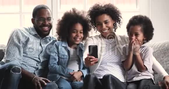 快乐的非洲父母和孩子在沙发上用电话笑视频的预览图