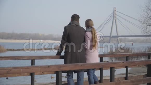 在城市公园站在桥上交谈的成年白种人夫妇的后景优雅的男人和女人看着河视频的预览图