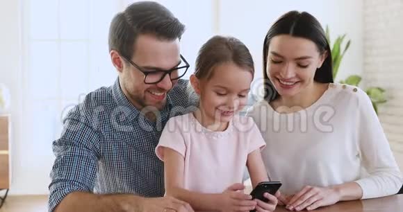 可爱的女儿拿着智能手机让父母看有趣的视频视频的预览图