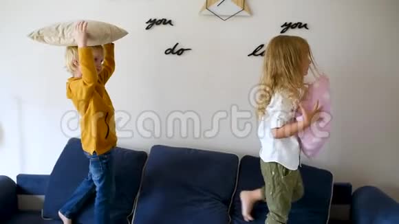 枕头大战淘气的学龄前儿童在沙发上跳跃用枕头互相撞击男孩和女孩一起玩视频的预览图