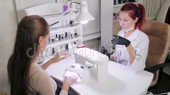 美容浴中的美甲医生正在客户指甲上涂胶那个女孩在紫外线灯里晒指甲视频的预览图