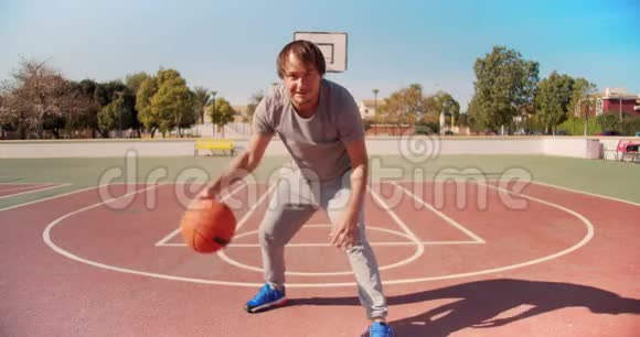 年轻的篮球运动员在运动服训练时拿着球看着外面篮球场上的镜头视频的预览图