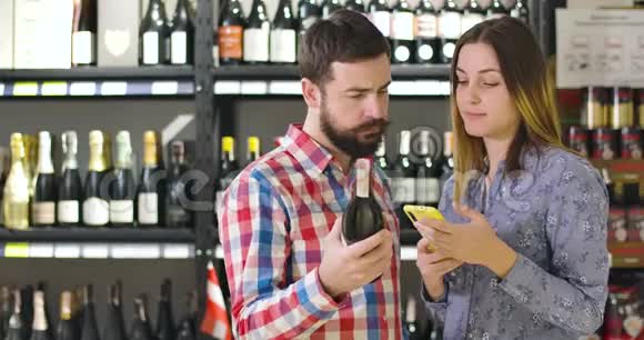 严肃的成年白种人男女比较酒瓶上的标签和电话中的信息现代夫妇核实视频的预览图