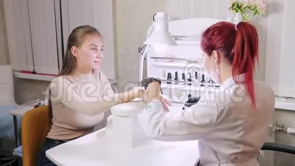 在美容院戴手套的女美甲师用湿毛巾擦拭顾客的指甲视频的预览图