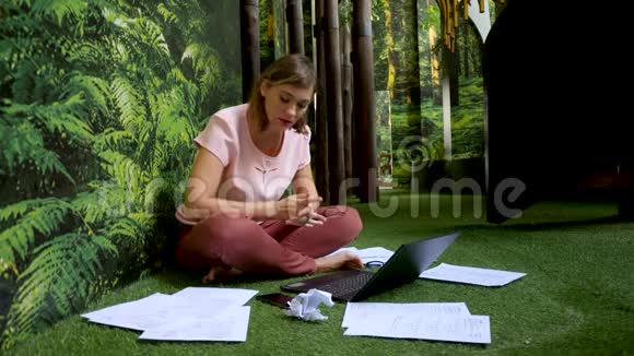 年轻迷人的女士坐在地板上打电话用笔记本电脑和文件加班视频的预览图