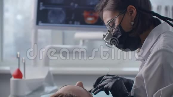 用双筒望远镜特写一位牙医在屏幕上图像背景的椅子上治疗一位病人视频的预览图