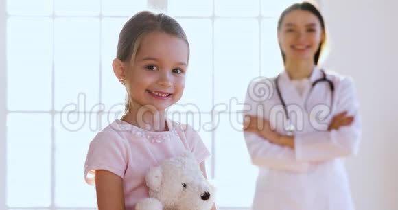 女儿科医生拥抱快乐可爱的女孩看镜头视频的预览图