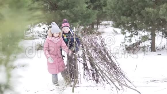冬天孩子们站在树林里的一间枯枝小屋视频的预览图