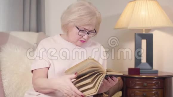 高加索金发女戴眼镜在家看书的肖像成熟聪明的女人在室内休息视频的预览图