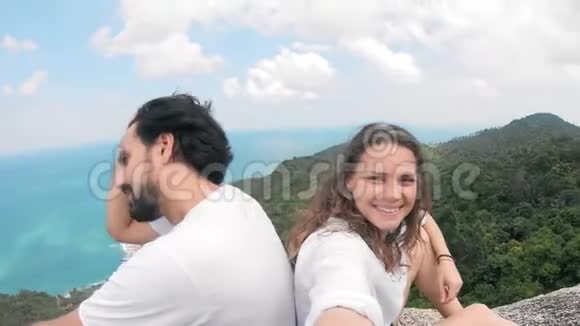 一对相爱的夫妇坐在山上看海景自拍视频的预览图