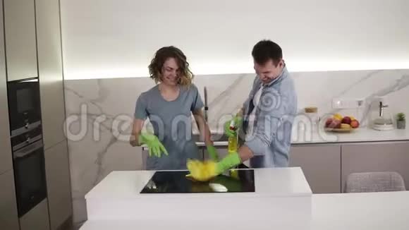 快乐的年轻夫妇在厨房跳舞两人都戴着绿色橡胶手套在工作室公寓的清洁日玩得很开心现代视频的预览图