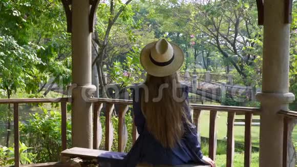 长发女子坐在夏季热带公园的长椅上视频的预览图
