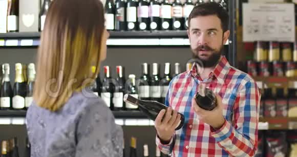 兴奋的年轻白种人男人拿着两瓶红酒和无法辨认的女人交谈的肖像自信视频的预览图