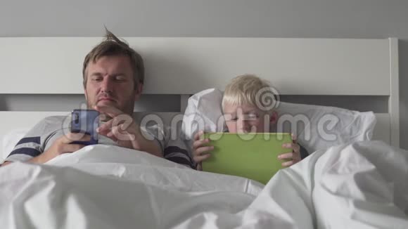 爸爸和儿子早上在床上玩平板电脑视频的预览图