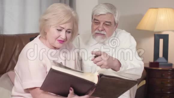 一对快乐的白人老夫妇在相册里看照片和谈话的肖像快乐的老年配偶视频的预览图