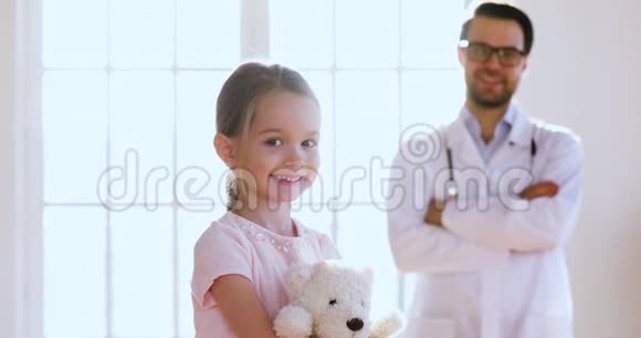 爱看的男儿科医生抱着小女孩看着摄像机视频的预览图