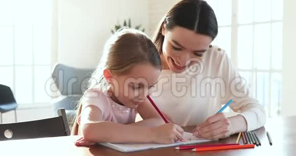 关爱的妈妈拥抱帮助的女儿用铅笔画画视频的预览图