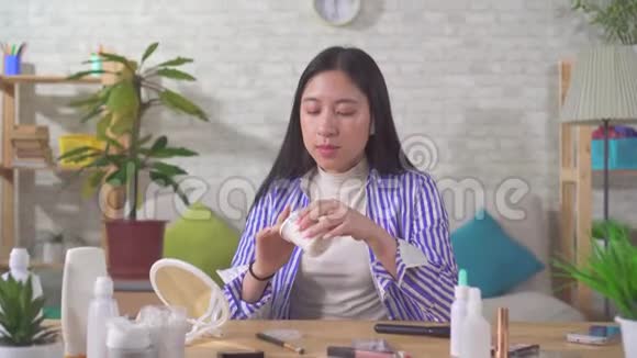 一个不满的年轻美丽的亚洲女人用面霜坐在家里的一张桌子上视频的预览图