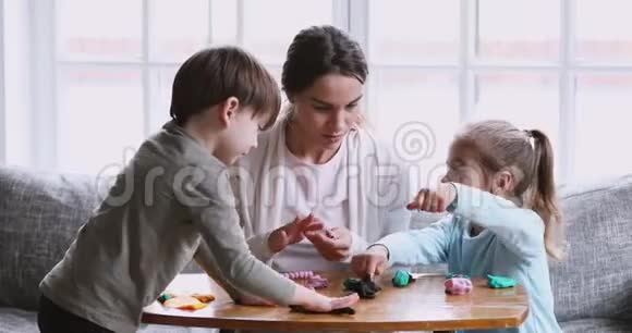 年轻的母亲和两个孩子在家里用泥塑模型视频的预览图