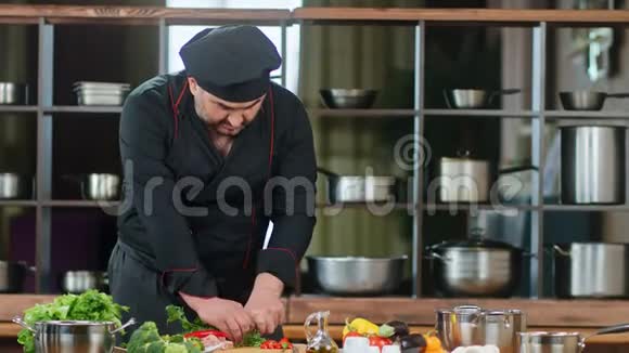 英俊的男厨师穿黑色制服切割绿色和胡椒中型摄影机视频的预览图