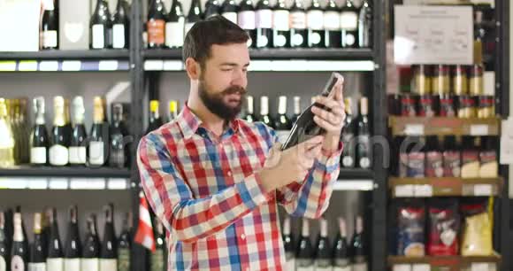 年轻开朗的白种人男人看着酒瓶上的标签拥抱着饮料看着相机微笑着满意视频的预览图