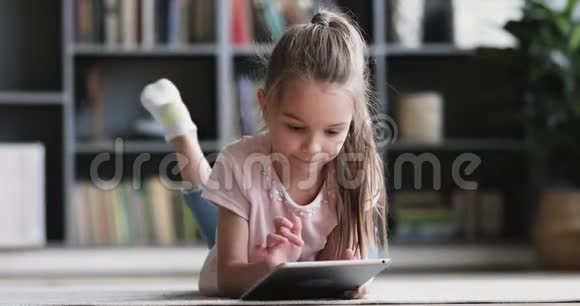 好奇可爱的学龄前女孩一个人用平板电脑躺在地毯上视频的预览图