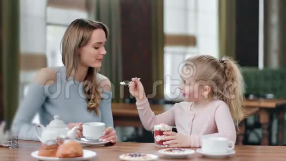可爱的顽皮的女儿用鲜奶油喂微笑的妈妈甜点中型摄影机视频的预览图