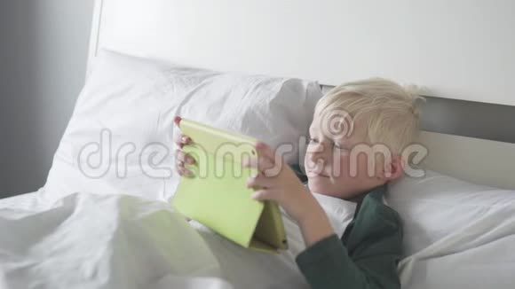 早上漂亮的金发男孩在平板电脑上玩游戏视频的预览图
