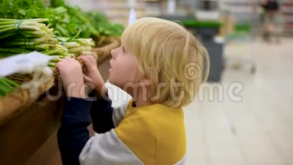 可爱的小男孩在食品商店或超市选择新鲜的有机绿色洋葱欧芹鳃生菜沙拉茴香韭菜视频的预览图
