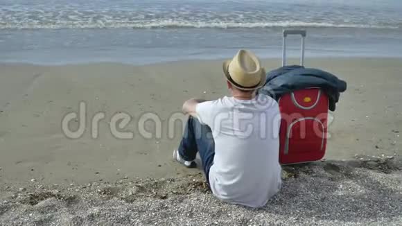 戴着帽子的游客坐在海滩上看着海浪视频的预览图