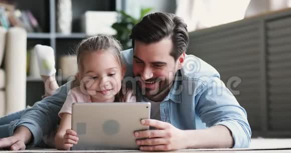 爸爸和小女儿用数字平板电脑躺在地上视频的预览图