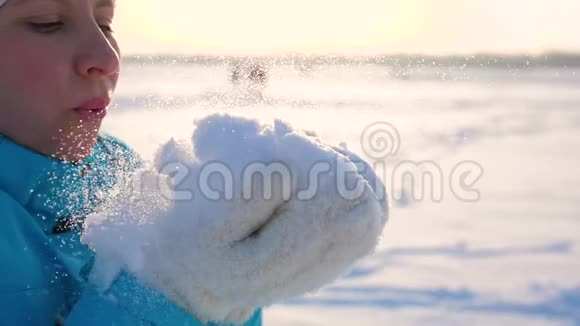 女孩在阳光明媚的背景下用手吹雪视频的预览图