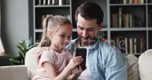 可爱的女儿学龄前儿童持有智能手机显示爸爸有趣的视频视频的预览图