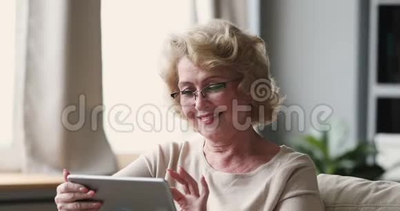 微笑的高级女士在家里用平板电脑戴眼镜视频的预览图