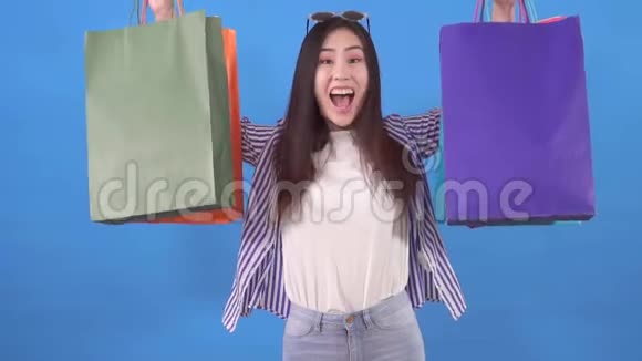 年轻的亚洲女人在蓝色背景的慢潮购物后拿着包裹视频的预览图