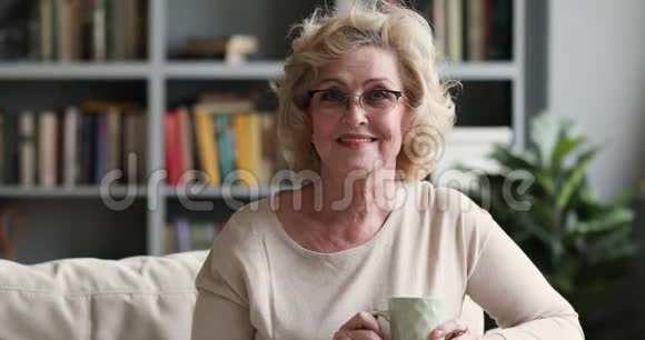幸福的老妇人坐在沙发上拿着茶杯画像视频的预览图
