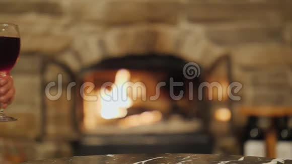 两只手拿着一杯酒在一个燃烧的壁炉的背景下叮当作响家里的节日和温馨视频的预览图