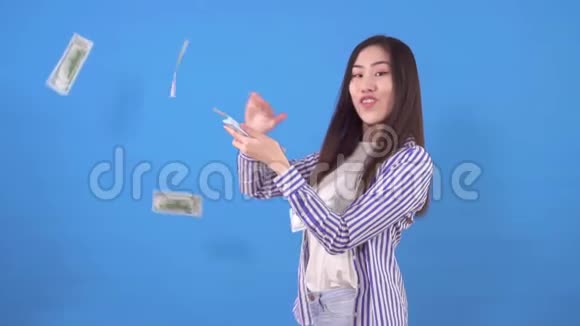 年轻漂亮的亚洲女人在蓝色背景上慢慢地把纸币美元撒开视频的预览图