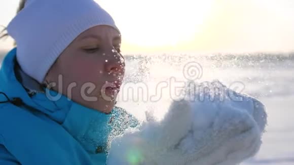 女孩在阳光明媚的背景下用手吹雪视频的预览图