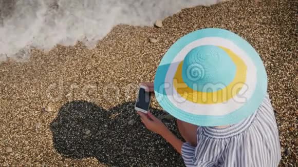一个戴着夏帽的女人坐在海滨拍摄石头和冲浪女人度假的概念视频的预览图