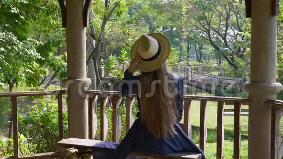 绿色夏日公园坐在长凳上戴草帽的游客妇女的后景视频的预览图