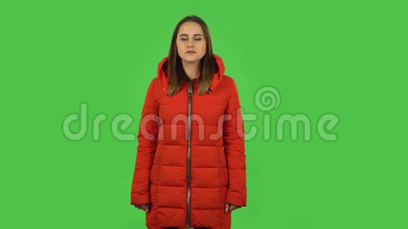 可爱的女孩穿着红色羽绒服看着相机微笑绿色屏幕视频的预览图