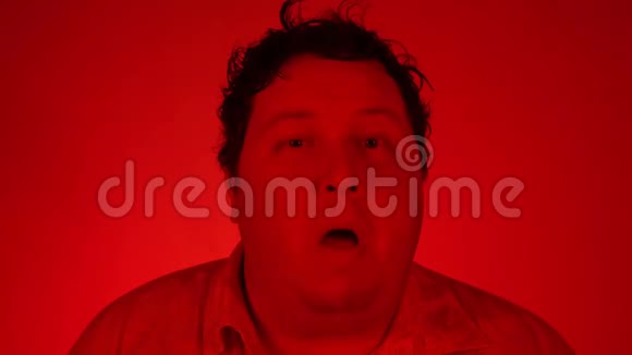 用红色灯光拍摄的肖像胖子站在红色背景上一边看镜头一边眨眼视频的预览图