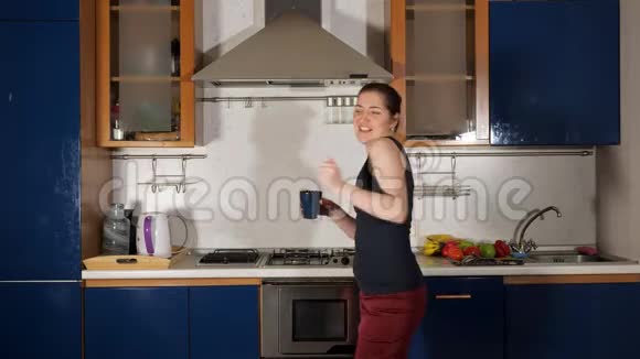 快乐的女孩在家里的厨房里跳舞喝茶唱歌视频的预览图