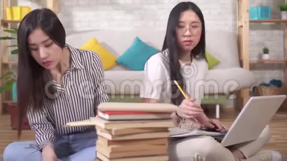 两个可爱的亚洲学生正在准备考试坐在书和笔记本电脑旁边的地板上视频的预览图