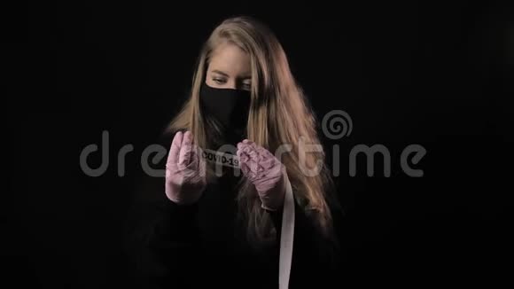 戴着黑色面具的女孩拿着一条丝带上面写着Covid19孤立在黑色背景上保健和医疗视频的预览图
